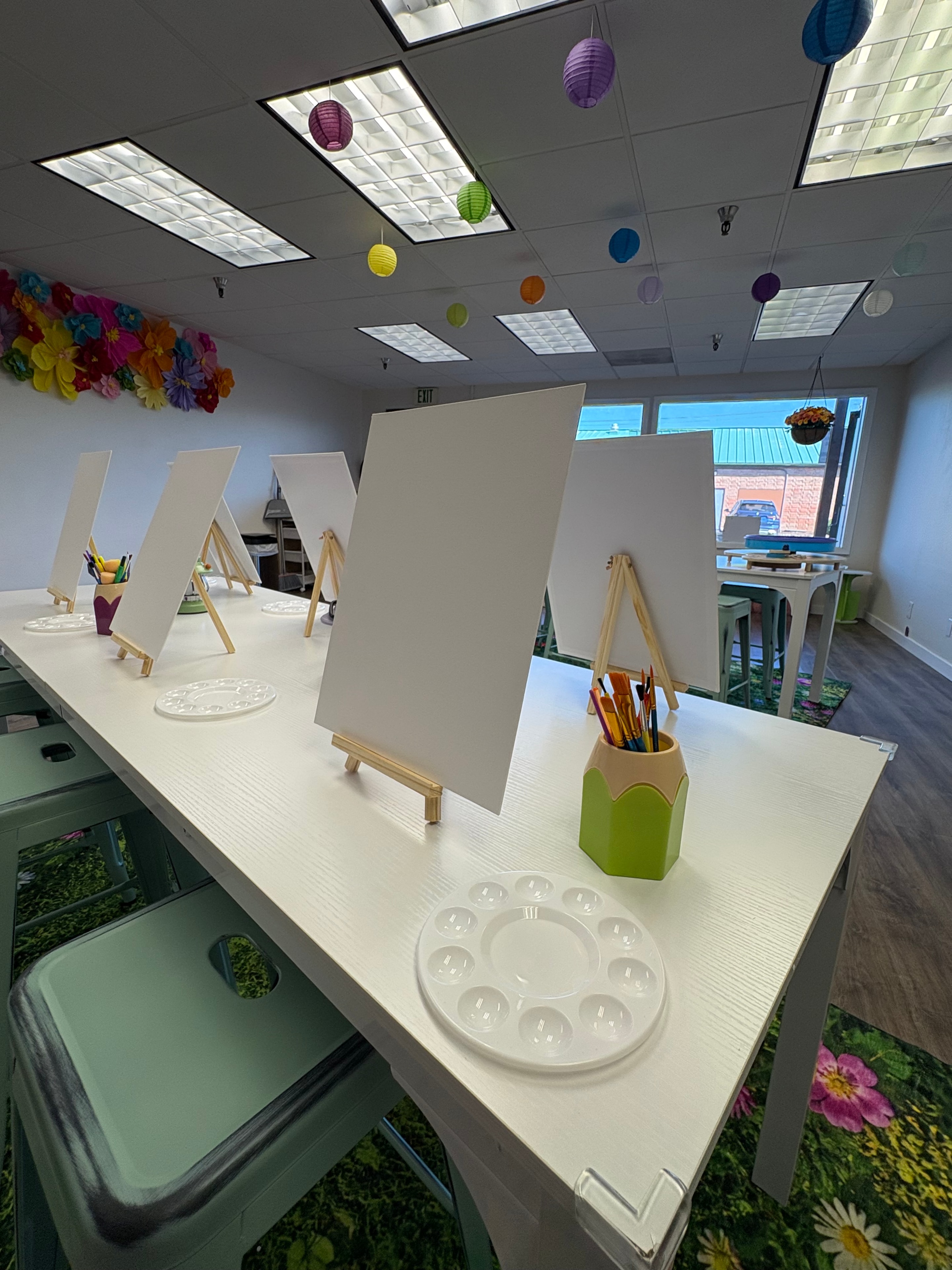 Art studio with easels, paint palettes, and colorful lanterns hanging from the ceiling