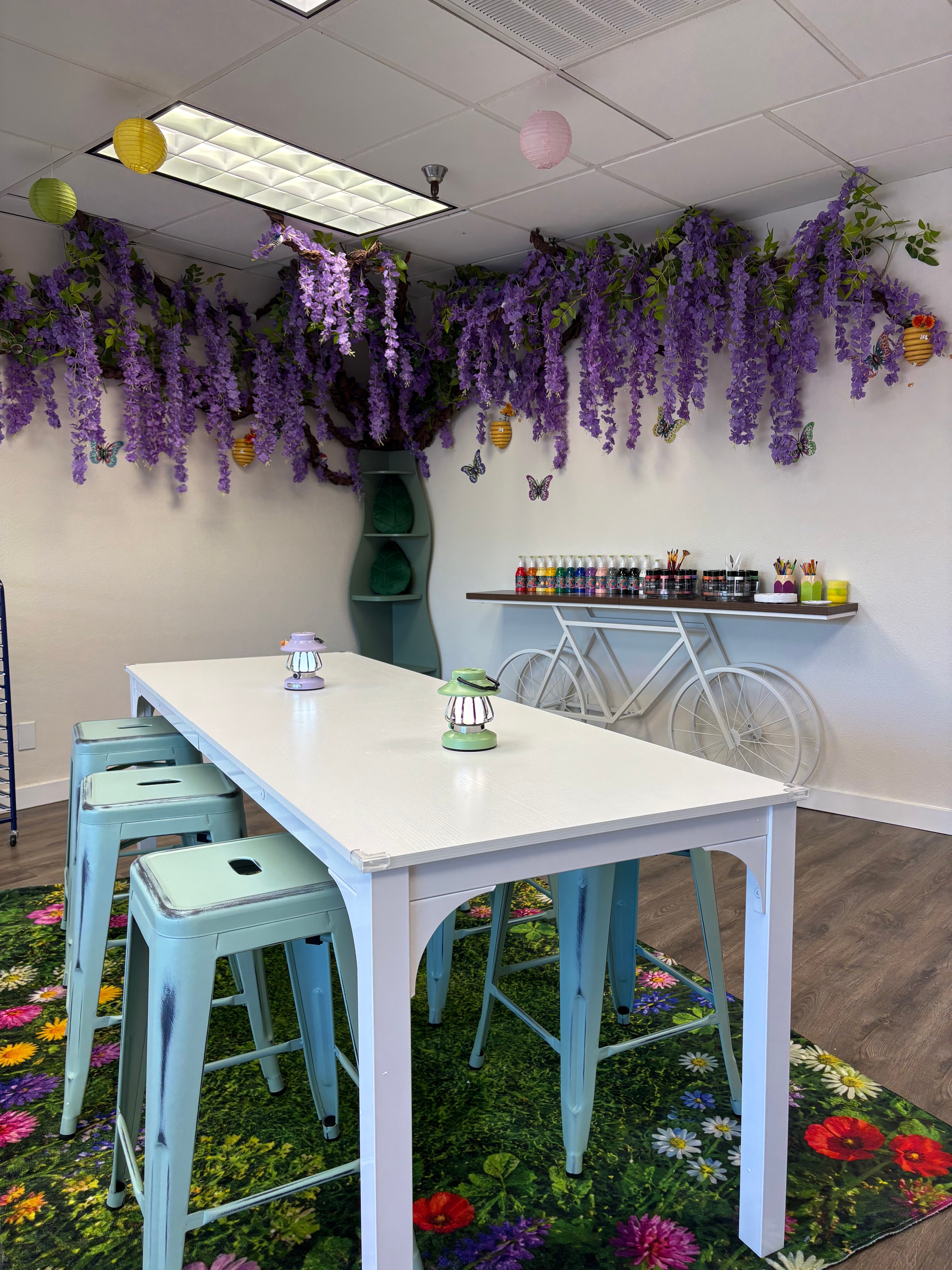Close-up of studio art table with wisteria wall, paint supplies, and teal stools