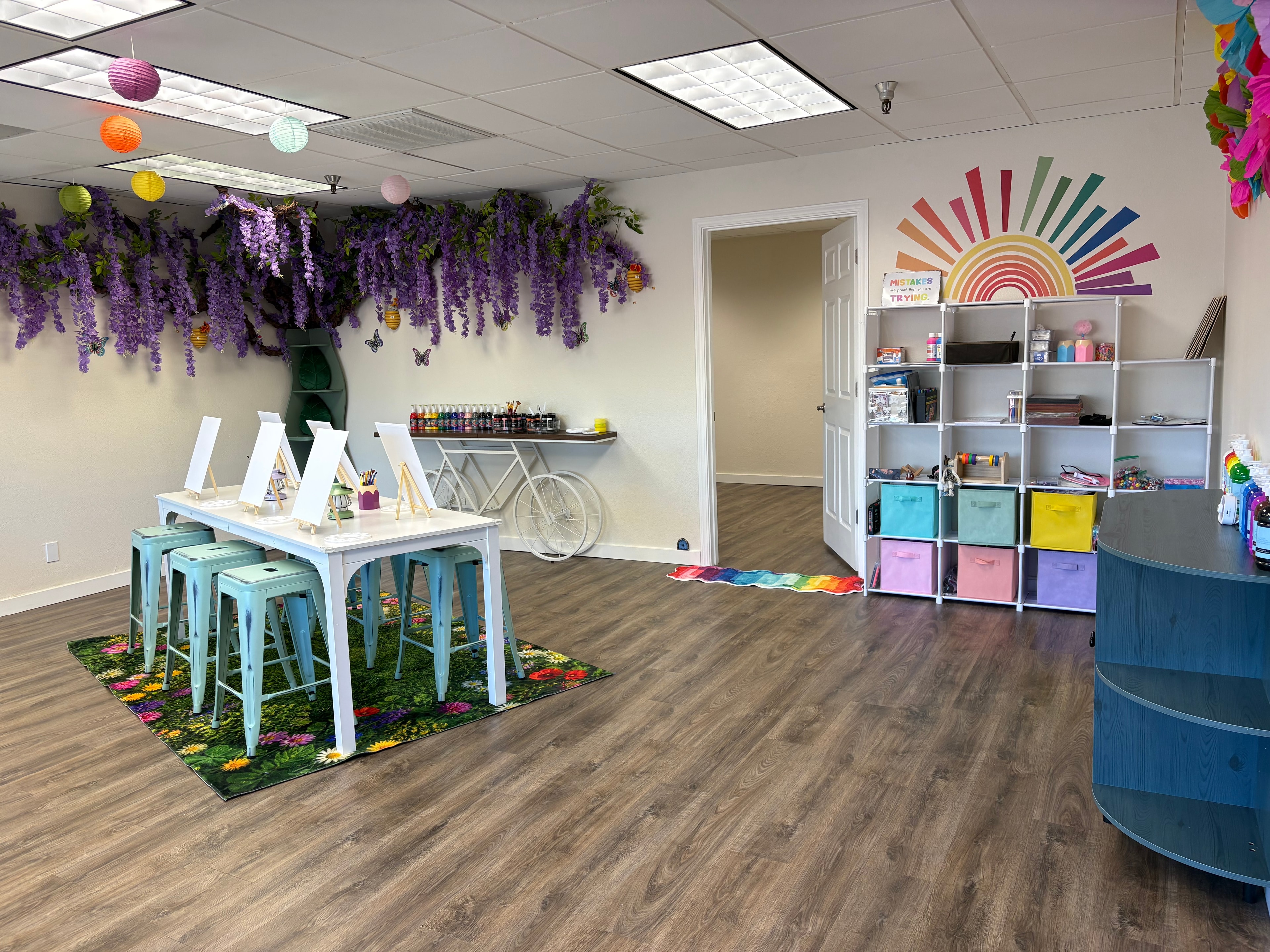 Full studio view with wisteria ceiling, easels set up at art table, and supply shelves