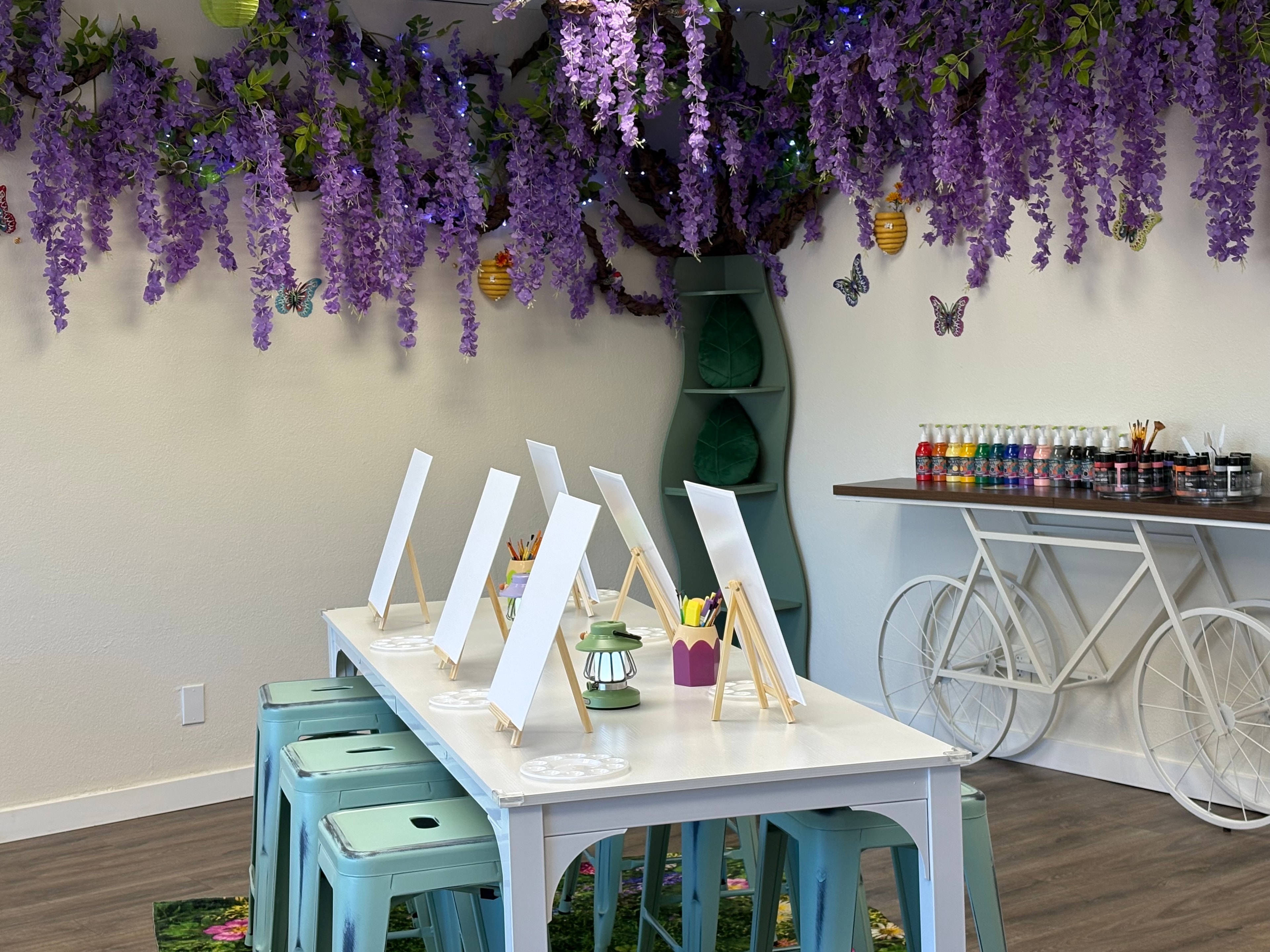 Studio art table with canvases on easels under wisteria and butterfly wall art